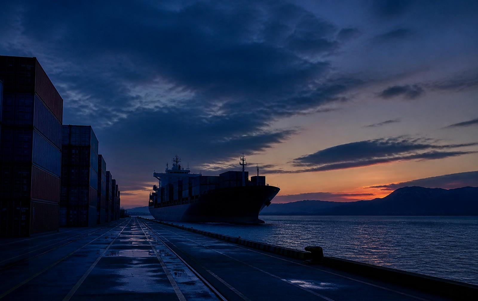 Container terminal at dusk with a cargo ship departing for a trans-Tasman crossing